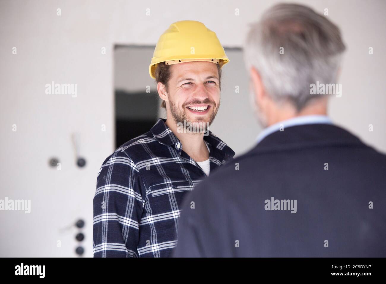 Smiling construction worker wearing hardhat talking with architect in constructing home Stock Photo