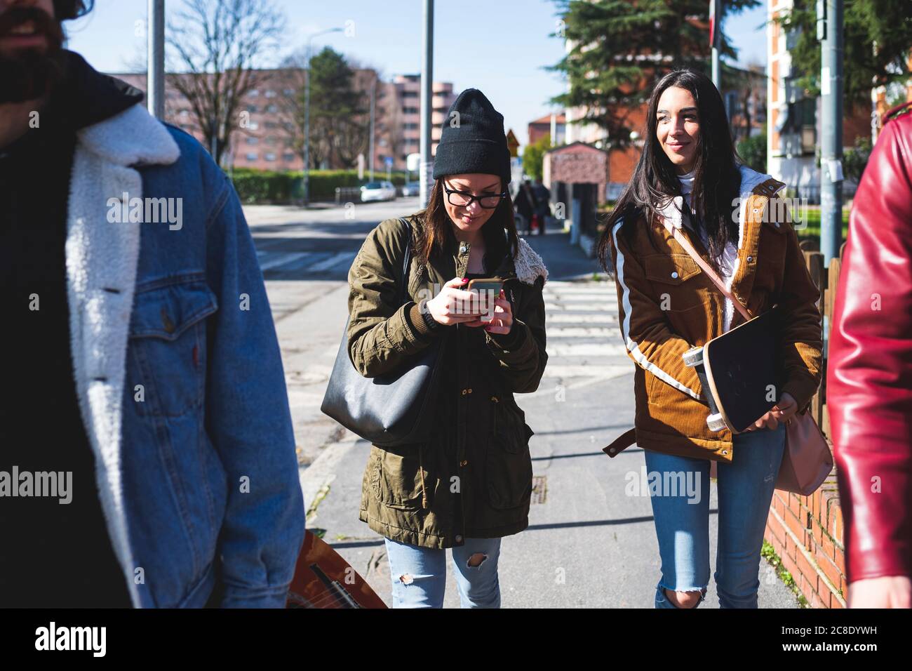 Woman using smart phone while walking with friends on sidewalk in city Stock Photo