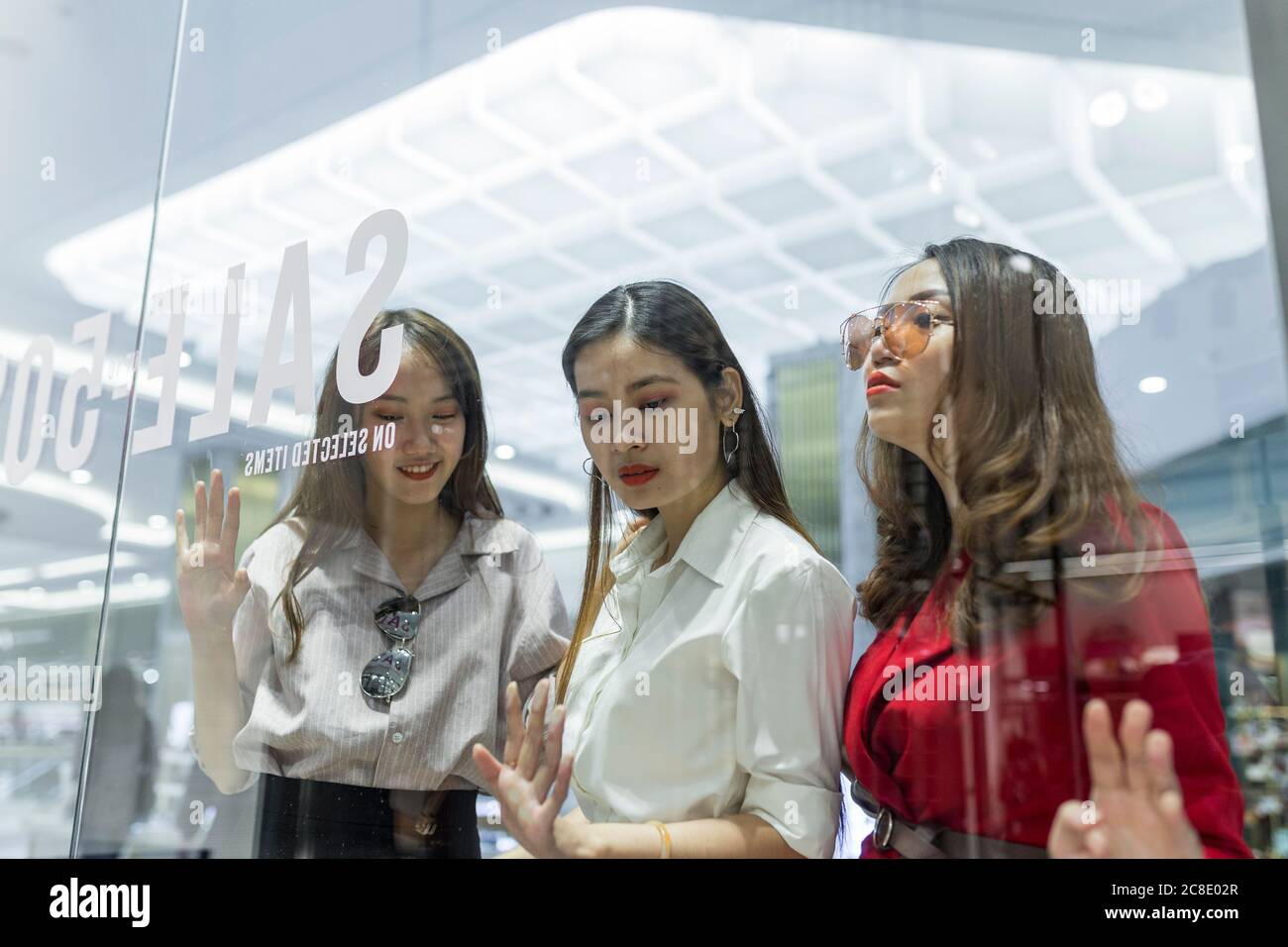 Female friends doing window shopping seen through glass in mall Stock Photo