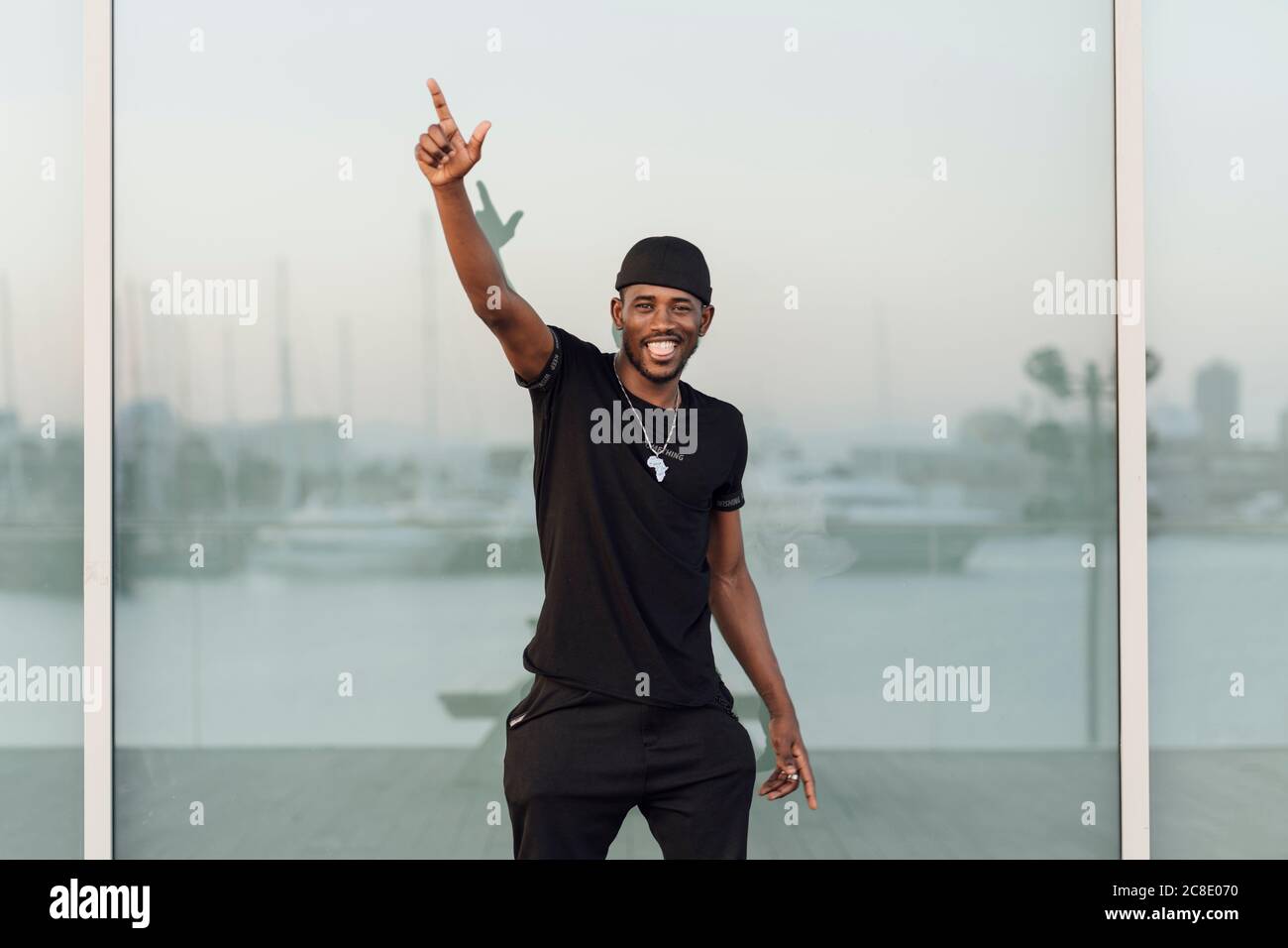 Smiling young man standing with arm raised against window Stock Photo