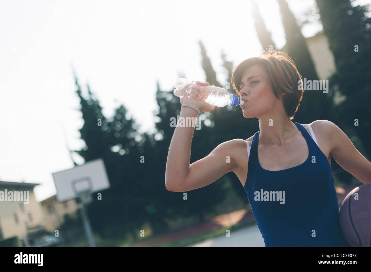 Teenage girl drinking water from bottle while holding basketball Stock Photo