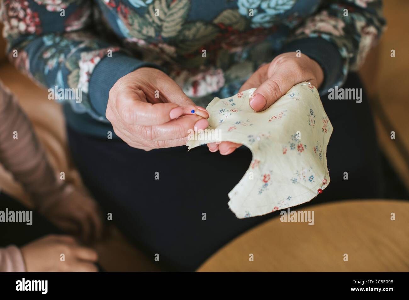 Mature woman holding straight pin and floral textile for sewing face mask at home Stock Photo