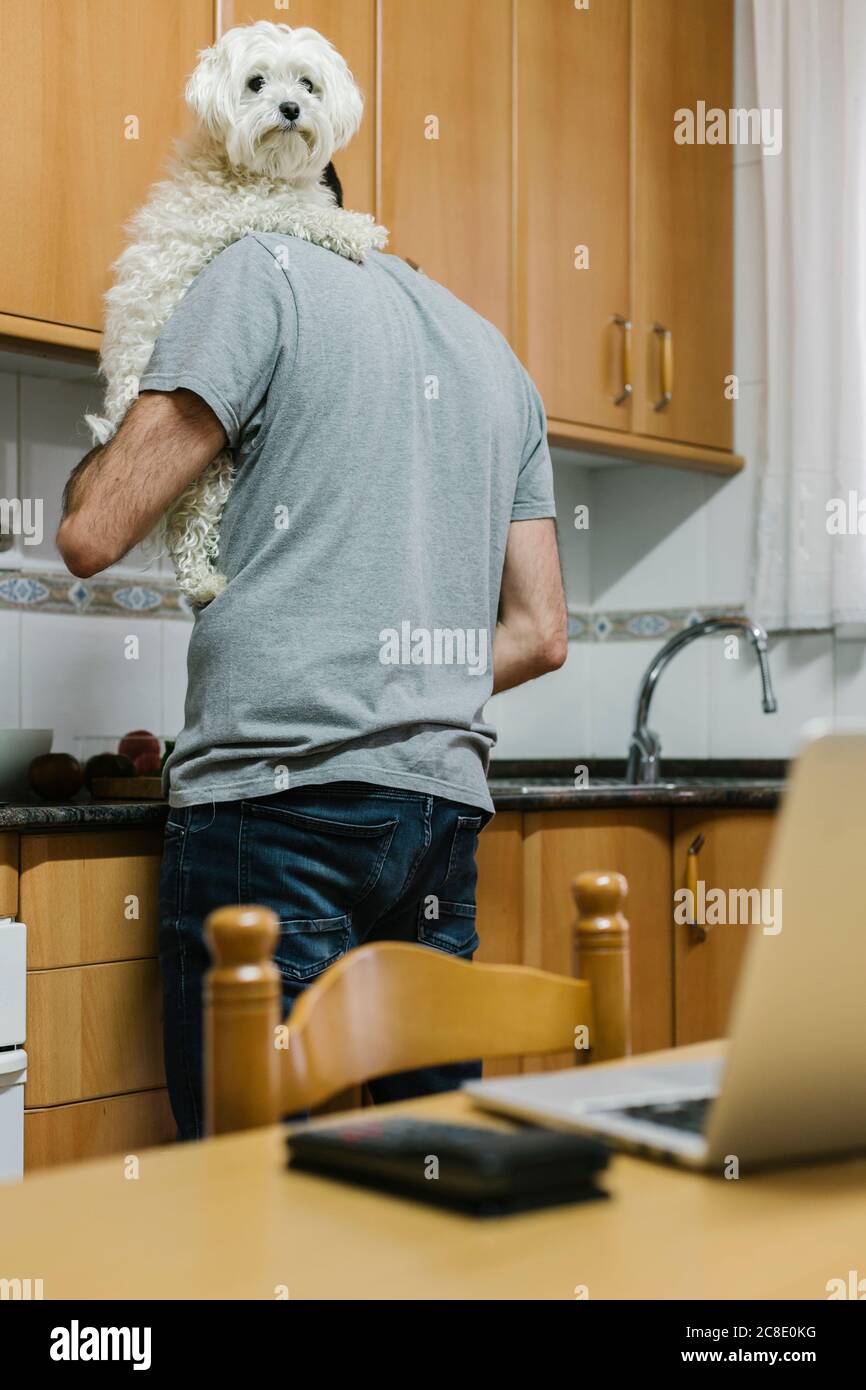Man carrying dog while cooking in kitchen Stock Photo