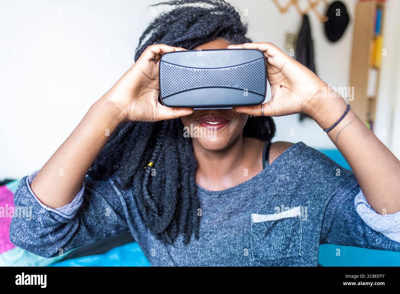 Young woman using virtual reality glasses sitting on bed Stock Photo
