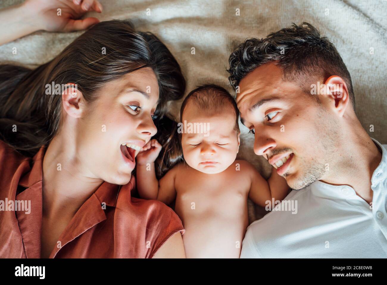 Cheerful parents lying with baby boy on bed at home Stock Photo