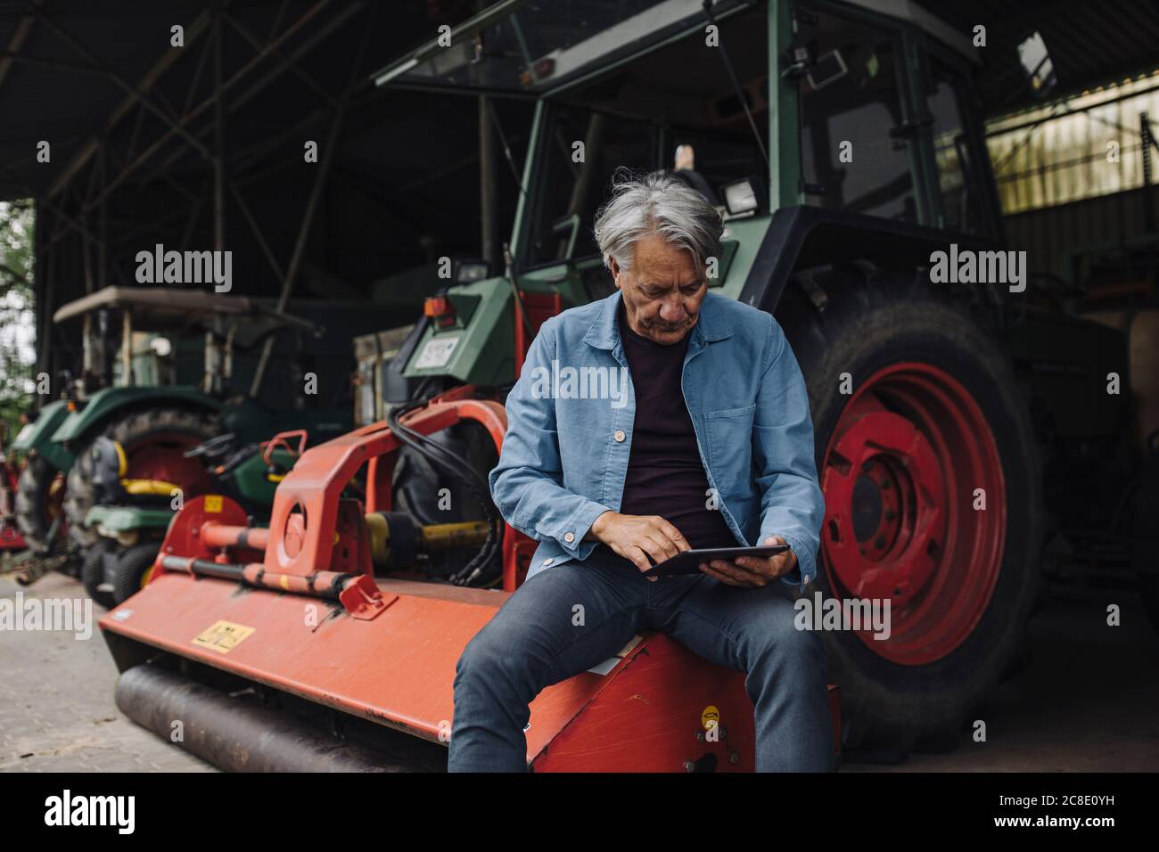 Senior man using tablet on a farm with tractor in barn Stock Photo