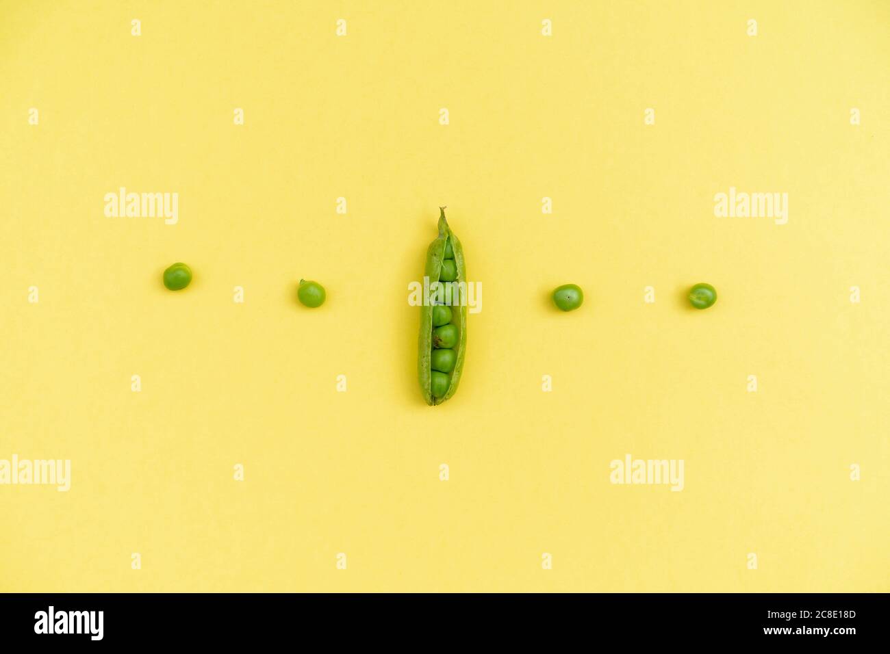 Studio shot of row of green peas and single pea pod against yellow background Stock Photo