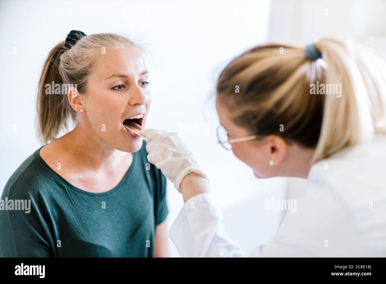 Female doctor examining female patient with tongue depressor Stock