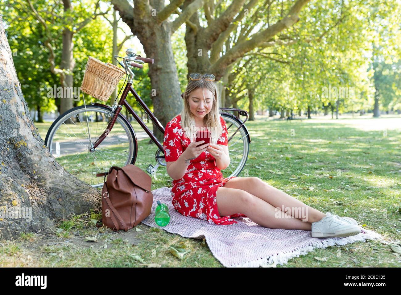 Woman using smart phone while sitting in public park Stock Photo