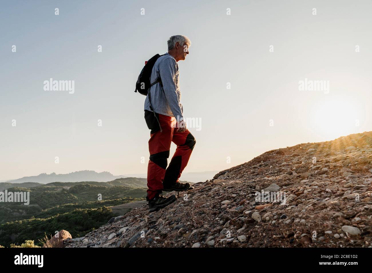 Active senior man hiking up on mountain against sky Stock Photo
