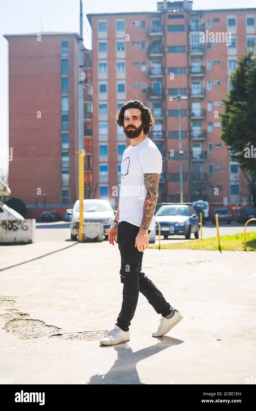 Bearded young man walking on road in city during sunny day Stock Photo