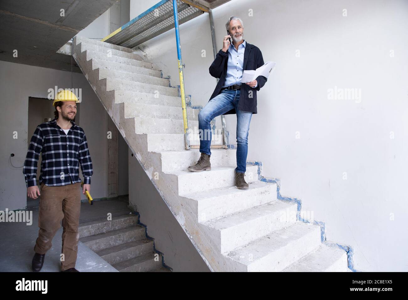 Male architect talking over smart phone while construction worker working in house under construction Stock Photo
