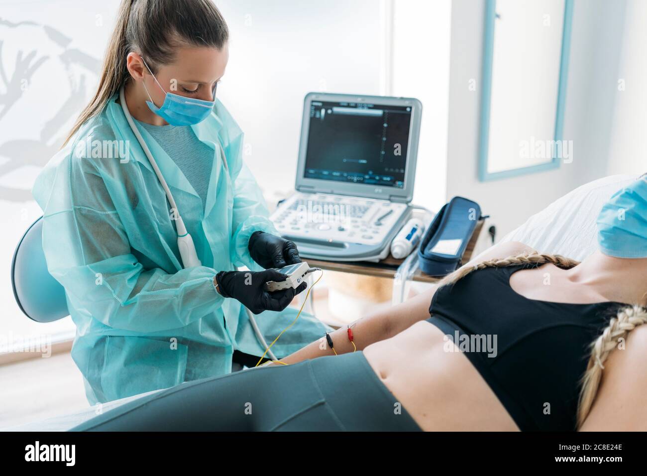 Doctor wearing face mask examining sportswoman with electrodes Stock Photo