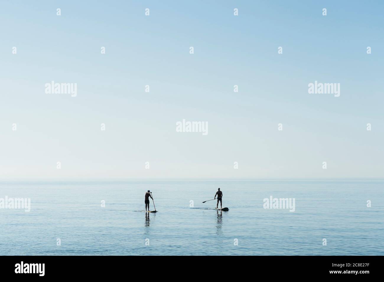 Mature men paddleboarding on sea against sky Stock Photo