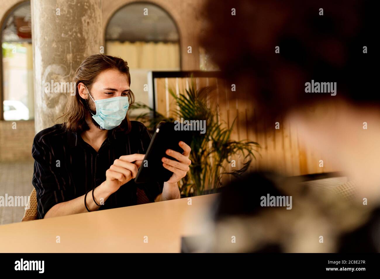 Young man wearing mask while sitting and using digital tablet in restaurant Stock Photo