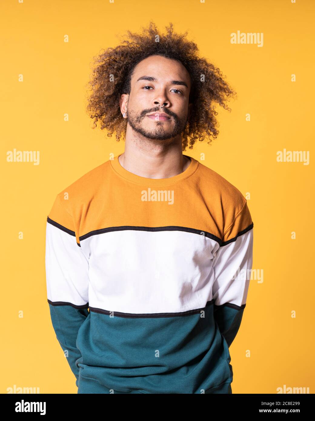 Handsome young man with curly hair standing against yellow background Stock Photo