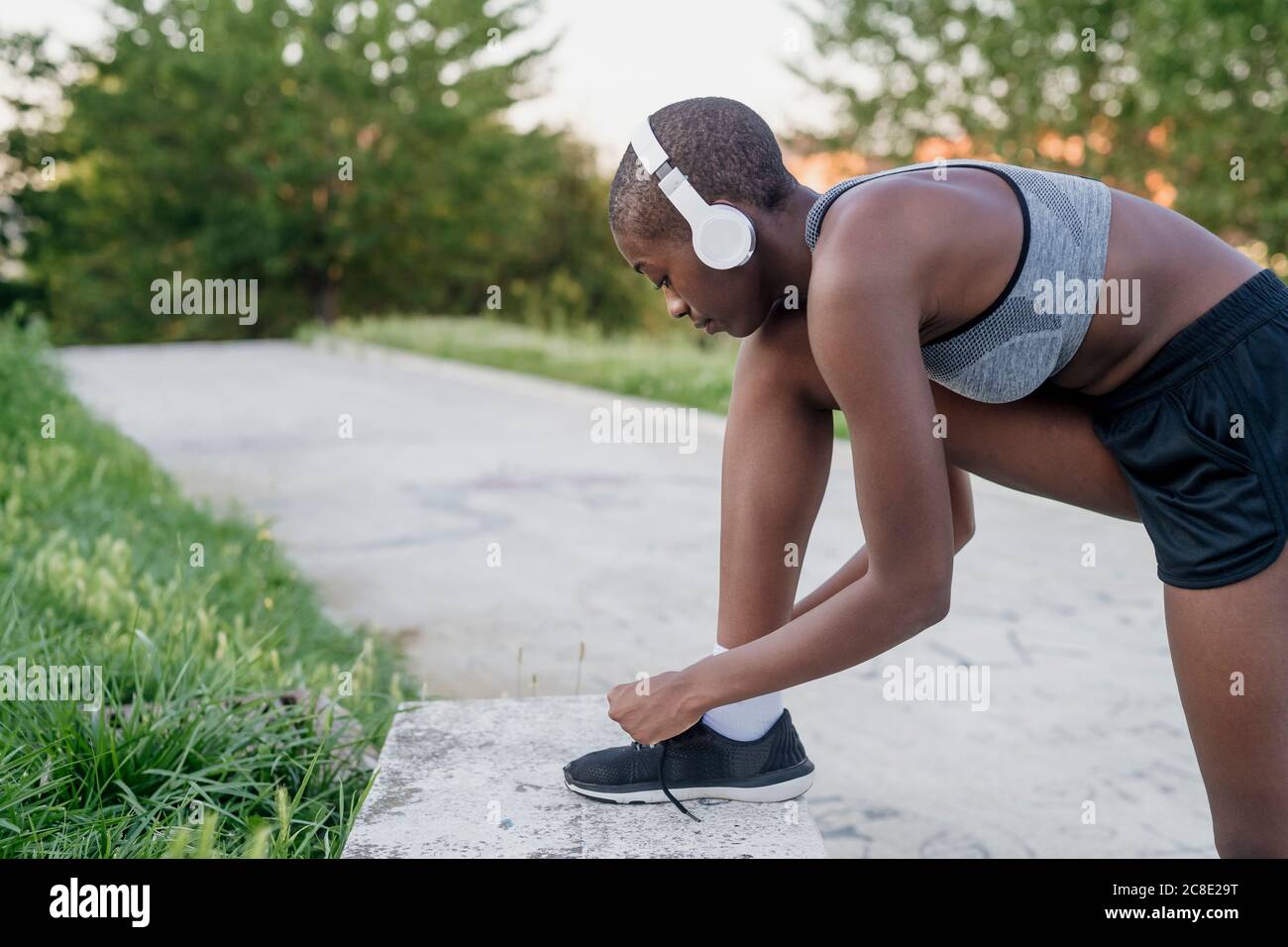 Female athlete wearing headphones tying shoelace on retaining wall in park Stock Photo