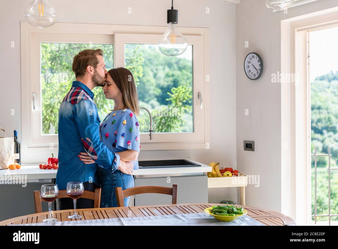 Man kissing woman while standing by dining table in kitchen at home Stock Photo