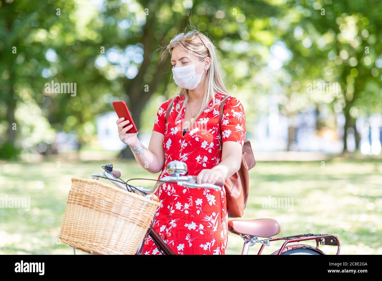 Woman with bicycle wearing mask while using smart phone at public park Stock Photo