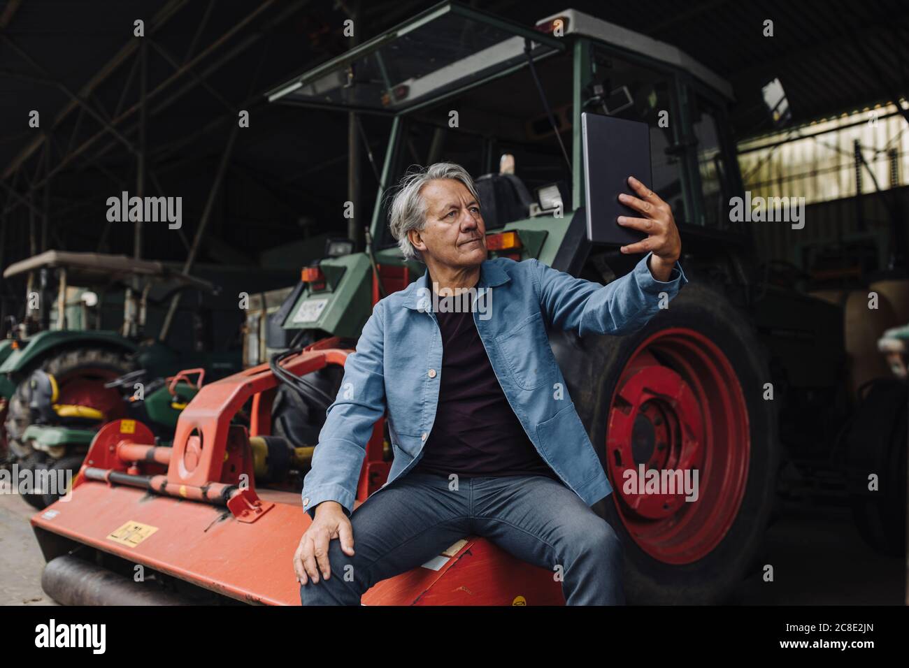 Senior man using tablet on a farm with tractor in barn Stock Photo