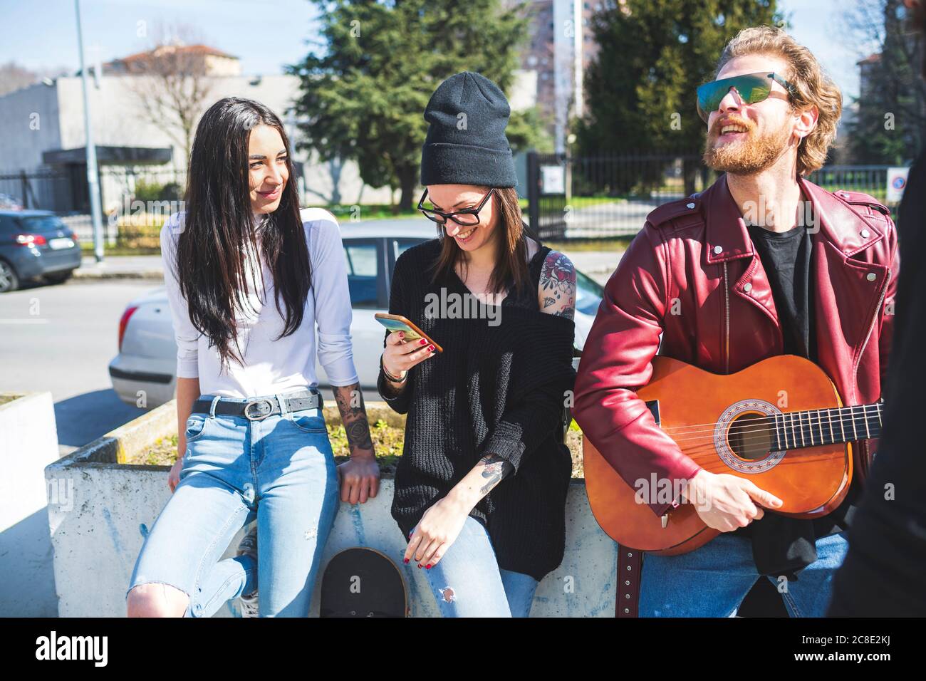 Bearded man playing guitar while standing with female friends in city Stock Photo