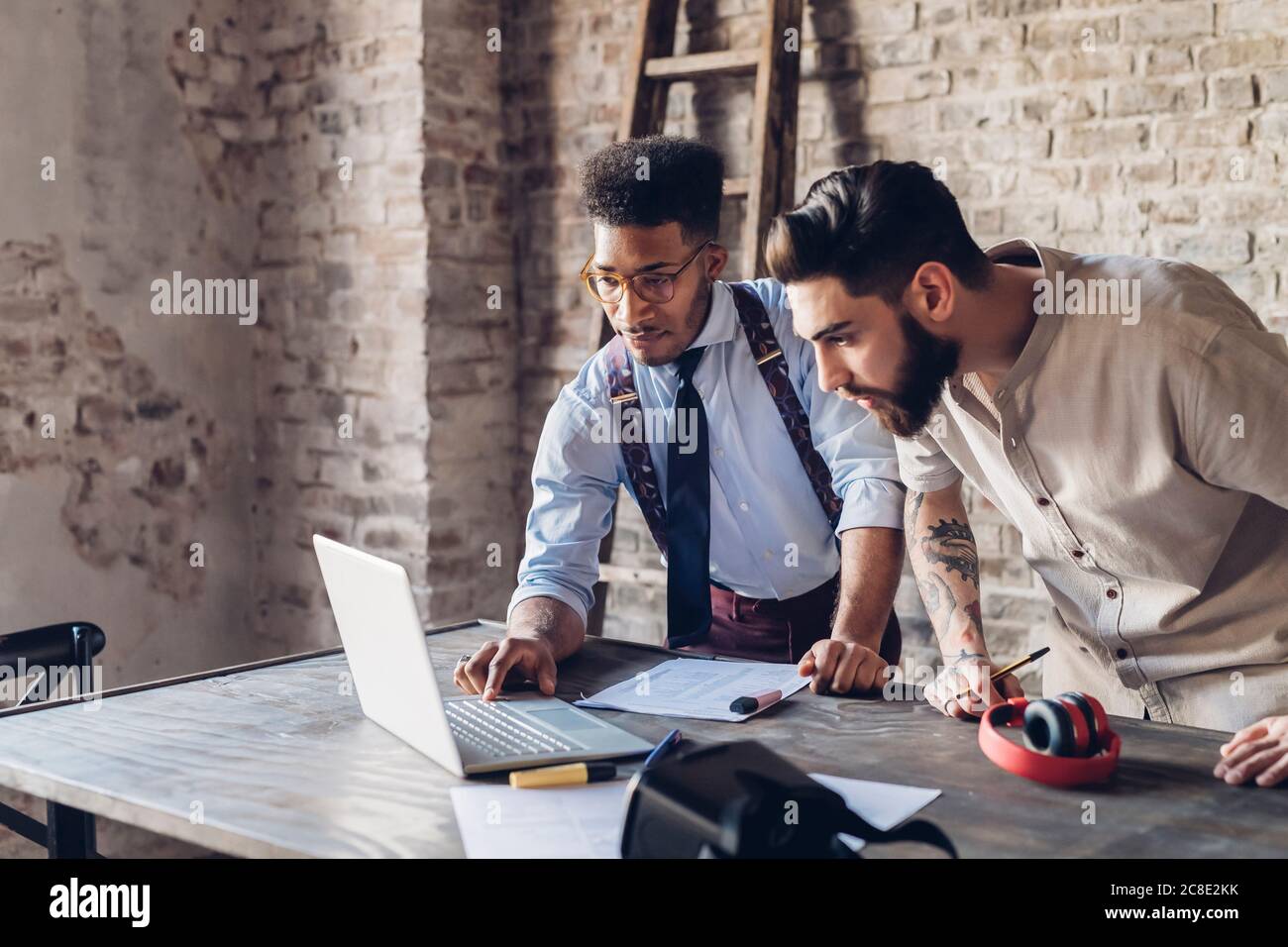 Two creative businessmen using laptop in loft office Stock Photo