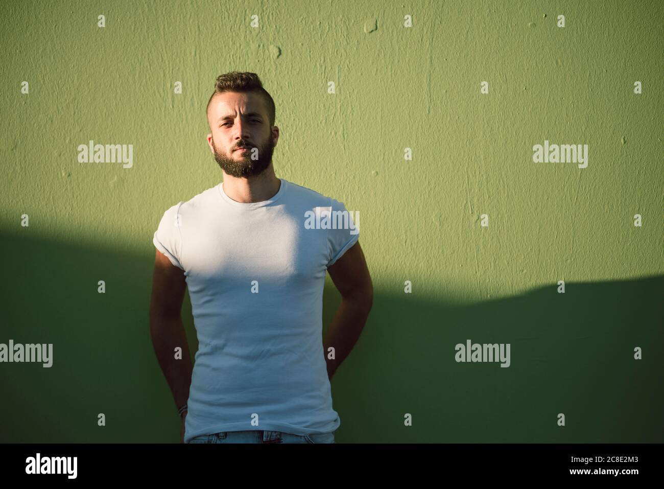 Confident young man standing against green wall Stock Photo - Alamy