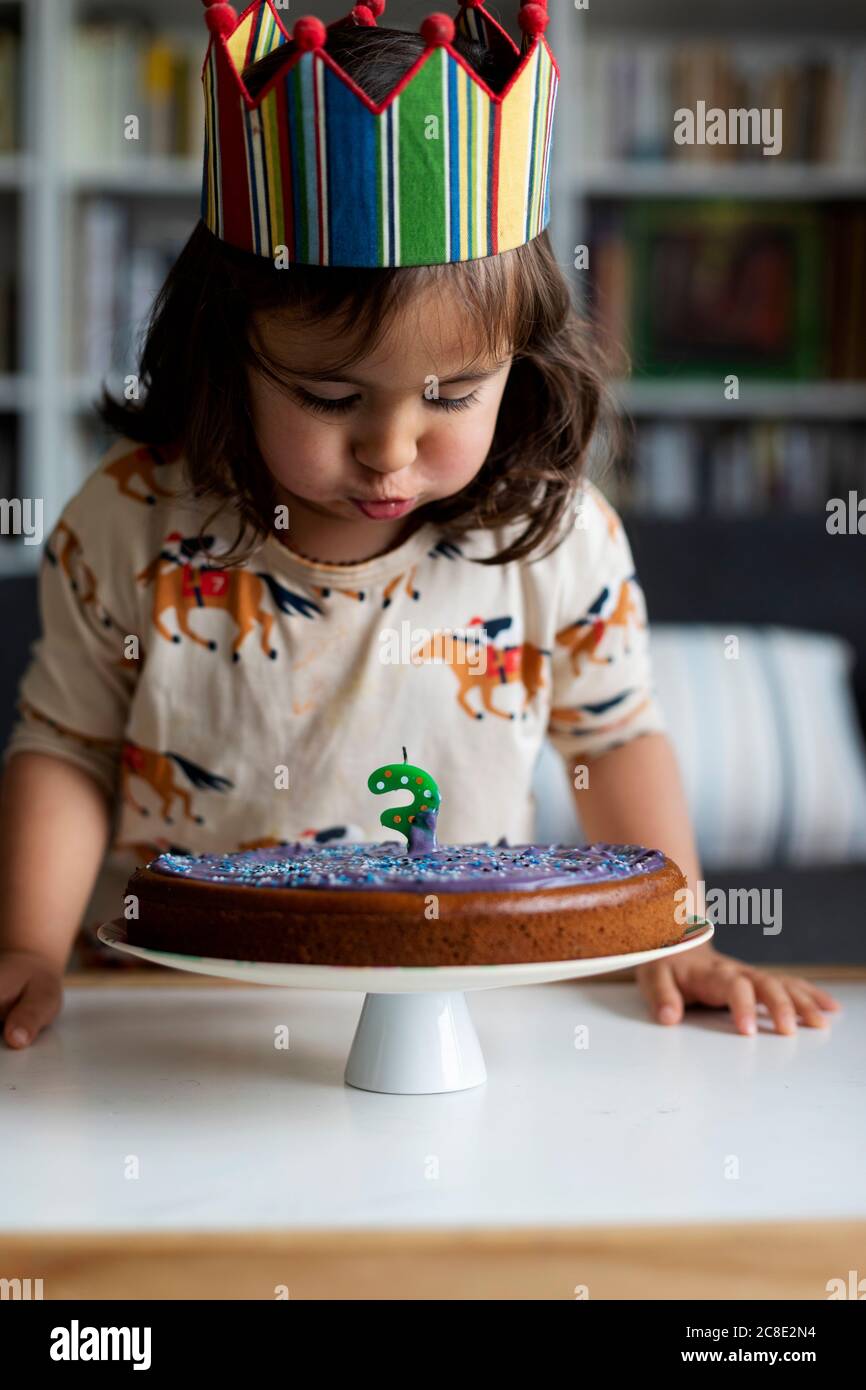 Portrait of little girl blowing out candle on her birthday cake at home