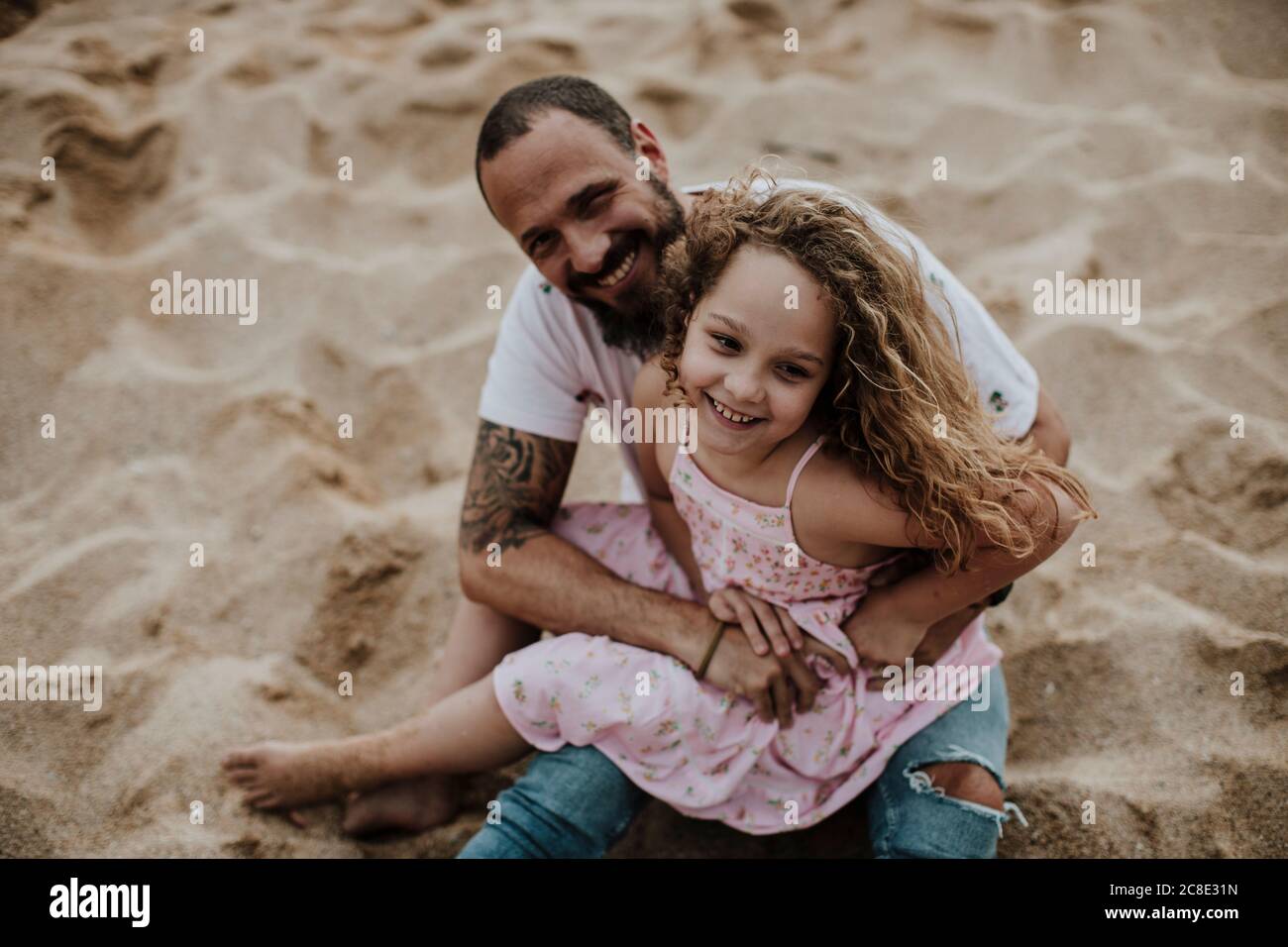Daughter sitting on father's lap while playing at beach Stock Photo