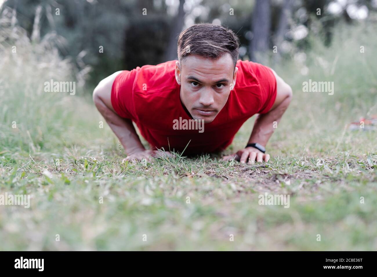 Man doing pushup on meadow, looking at camera Stock Photo