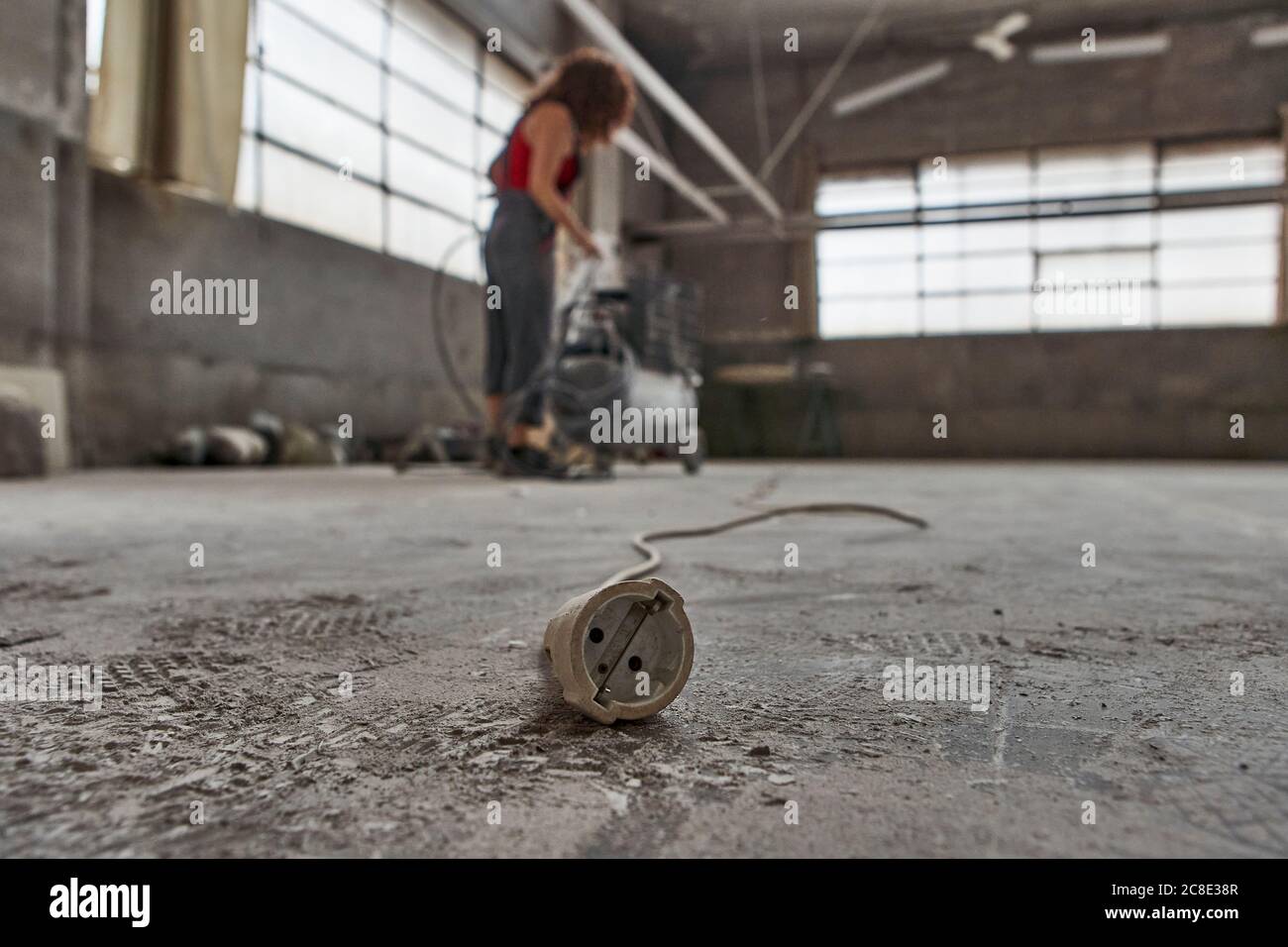 Close-up of cable on floor with woman hauling compressor in background at workshop Stock Photo