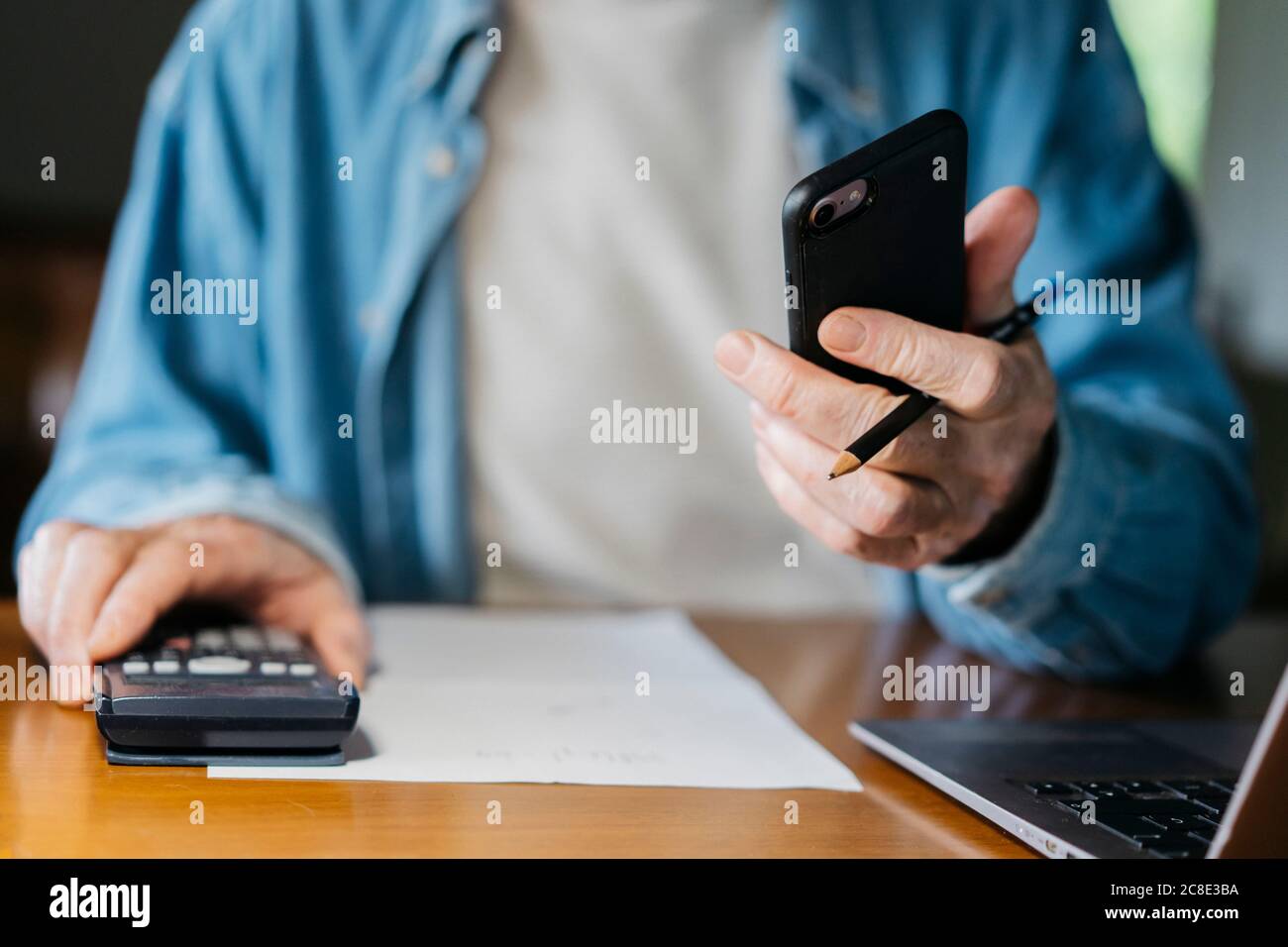 Senior man holding smart phone while using calculator and laptop at home Stock Photo