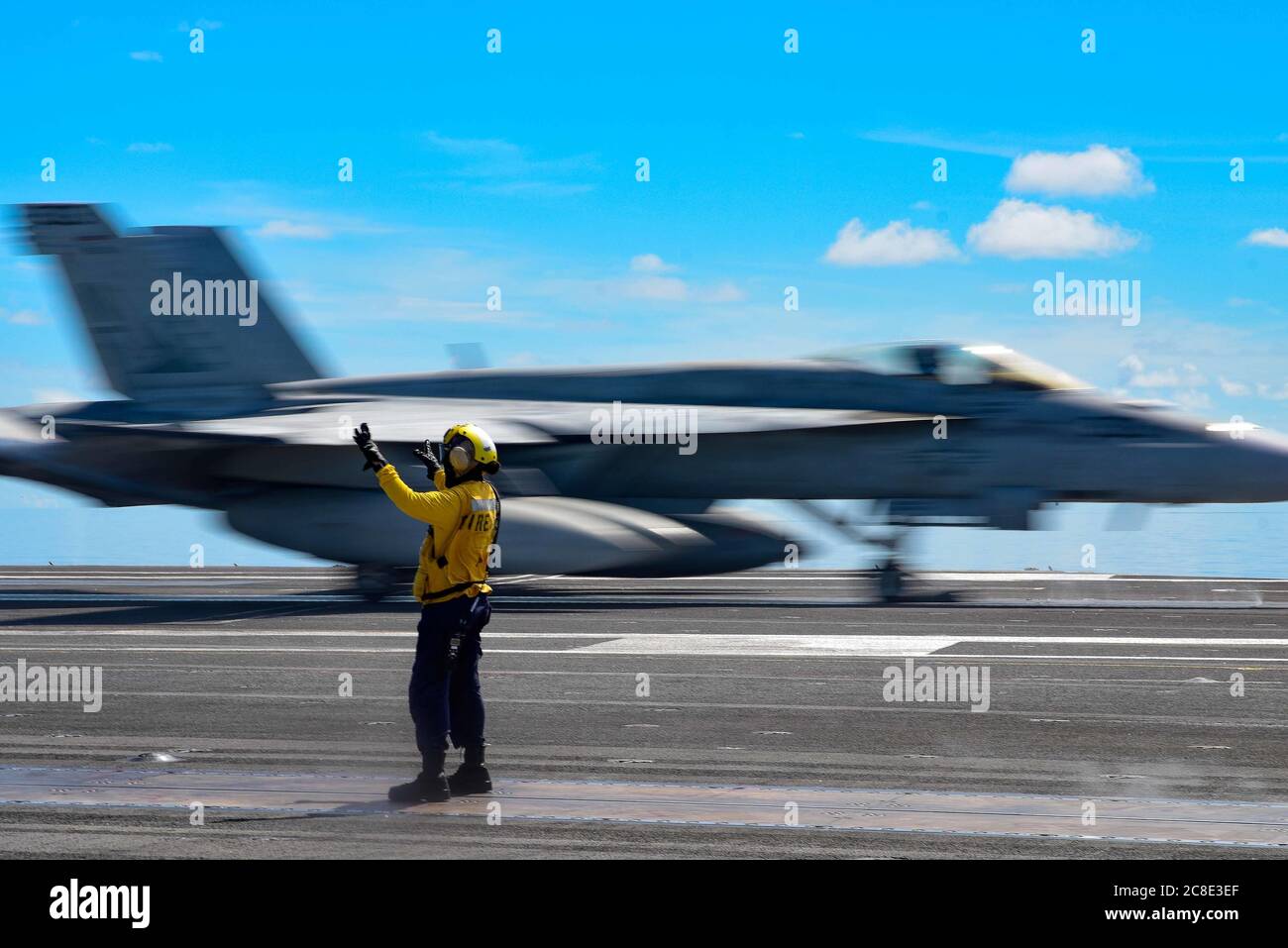 A U.S. Navy deck crew member signals a F/A-18E Super Hornet fighter aircraft, attached to Eagles of Strike Fighter Squadron 115, for launch on the flight deck of the Nimitz-class aircraft carrier USS Ronald Reagan July 17, 2020 underway in the South China Sea. Stock Photo