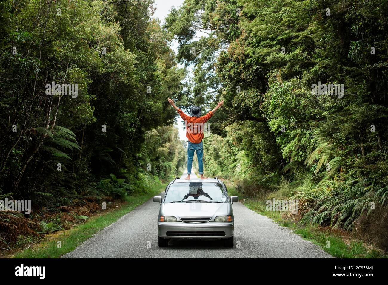Young man with arms outstretched standing on car roof at country road