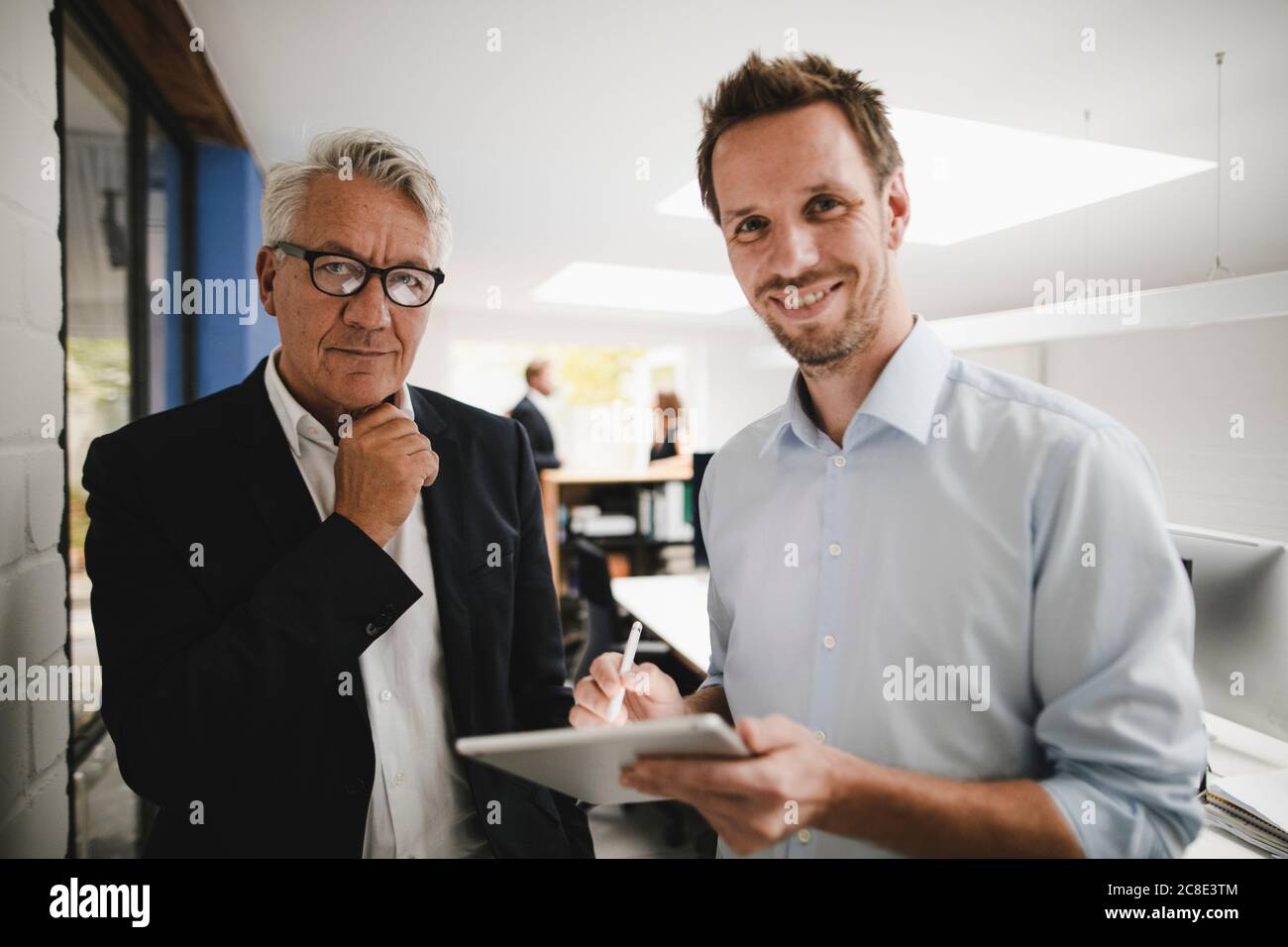 Two successful businessmen standing in office, using digital tablet Stock Photo