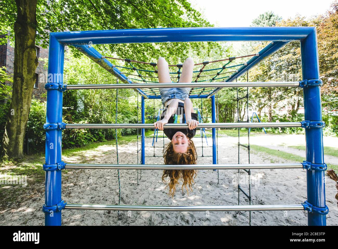 Smiling girl hanging upside down on jungle gym in playground at park Stock Photo