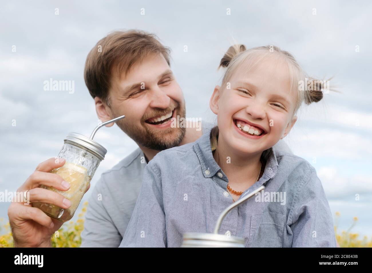Smiling man and daughter enjoying lemonade against sky Stock Photo