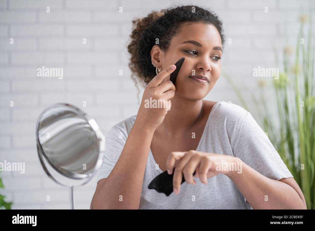 Close-up of young woman massaging face with gua sha stone at home Stock Photo