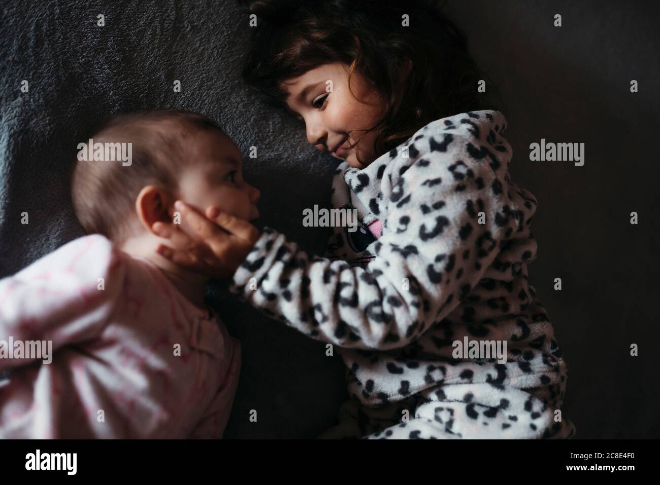 Girl touching baby sister's cheeks while lying on bed at hone Stock Photo
