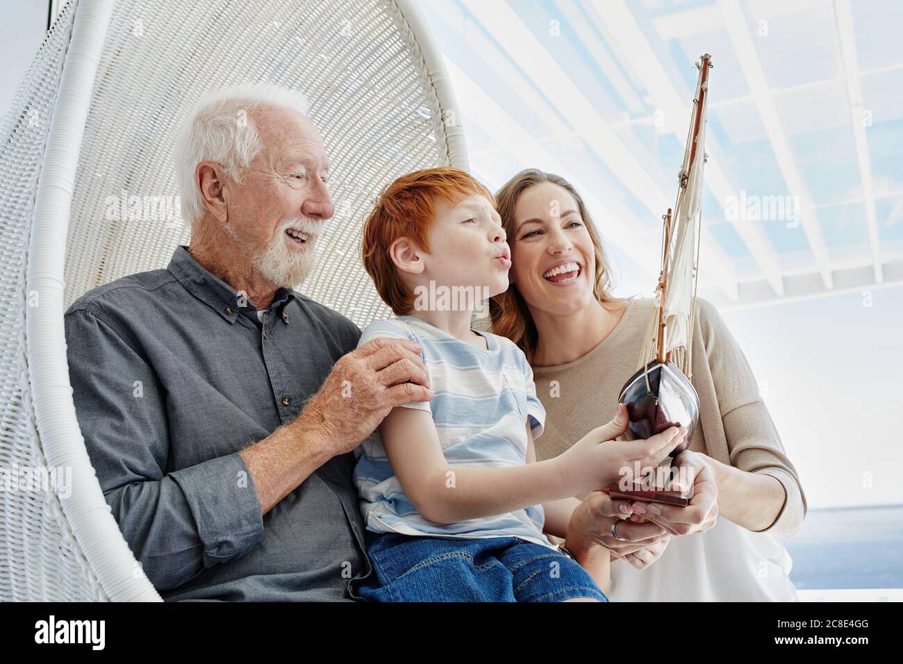Happy grandfather, mother and son with model sailing ship in hanging chair Stock Photo