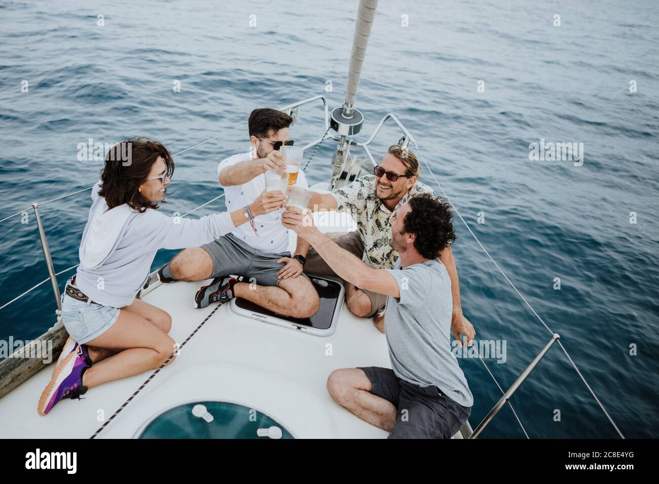 Carefree friends toasting beer glasses while sitting on sailboat in sea Stock Photo