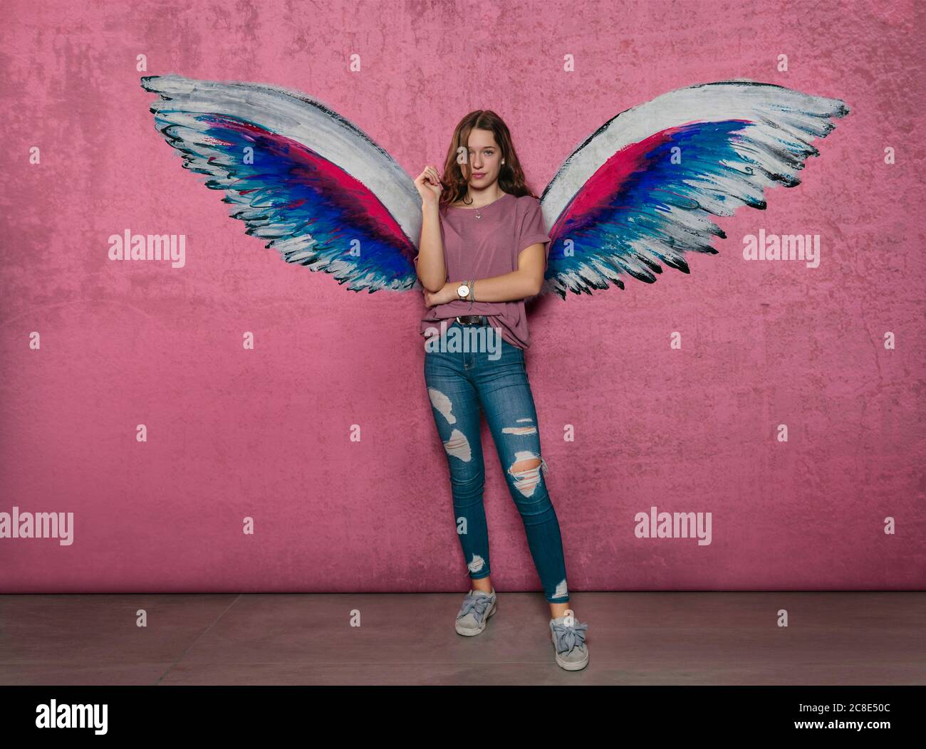 Teenage girl standing against angel wings graffiti on pink wall Stock Photo