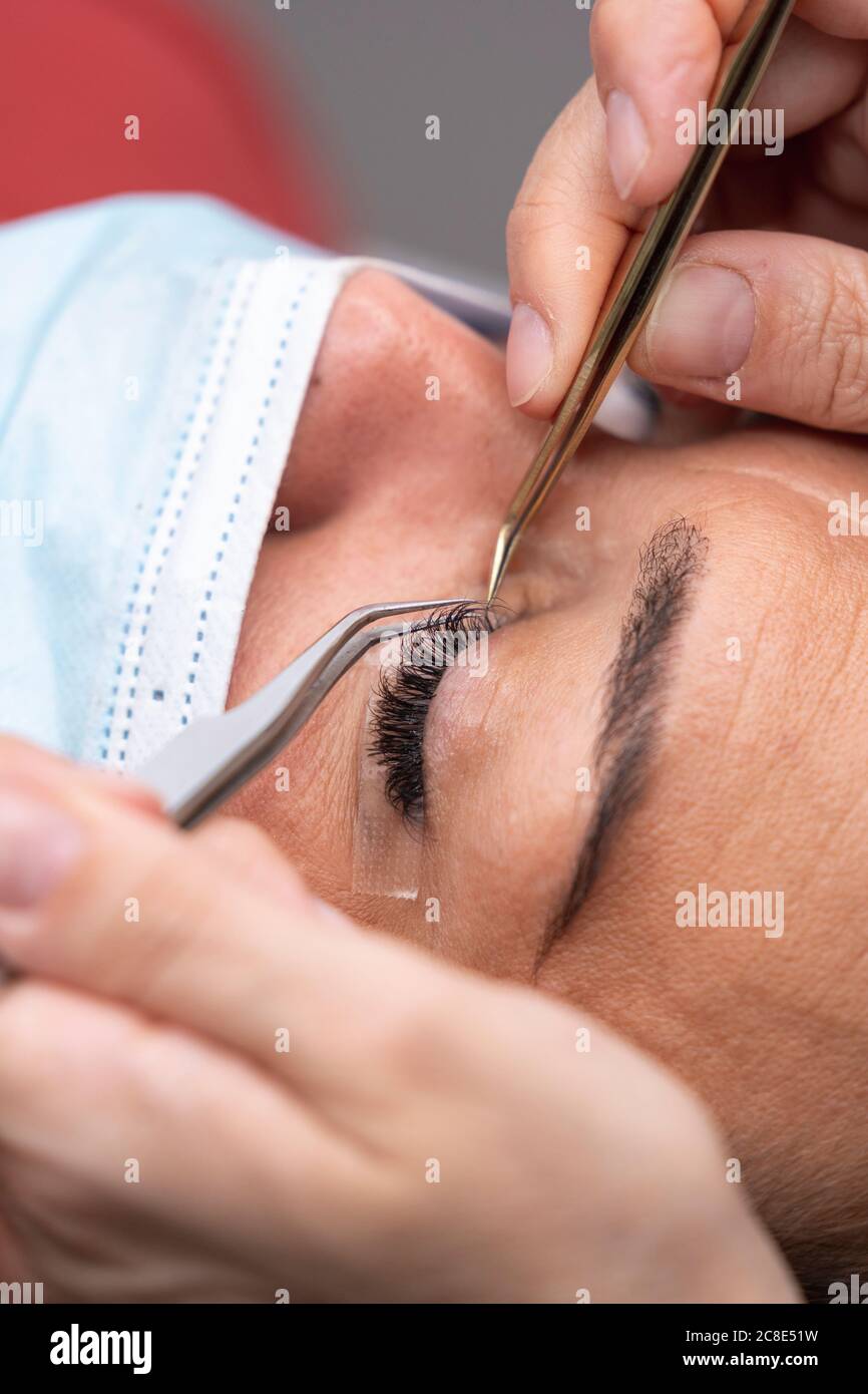 Hands of beautician using tweezers on customer for eyelash extension at beauty spa Stock Photo