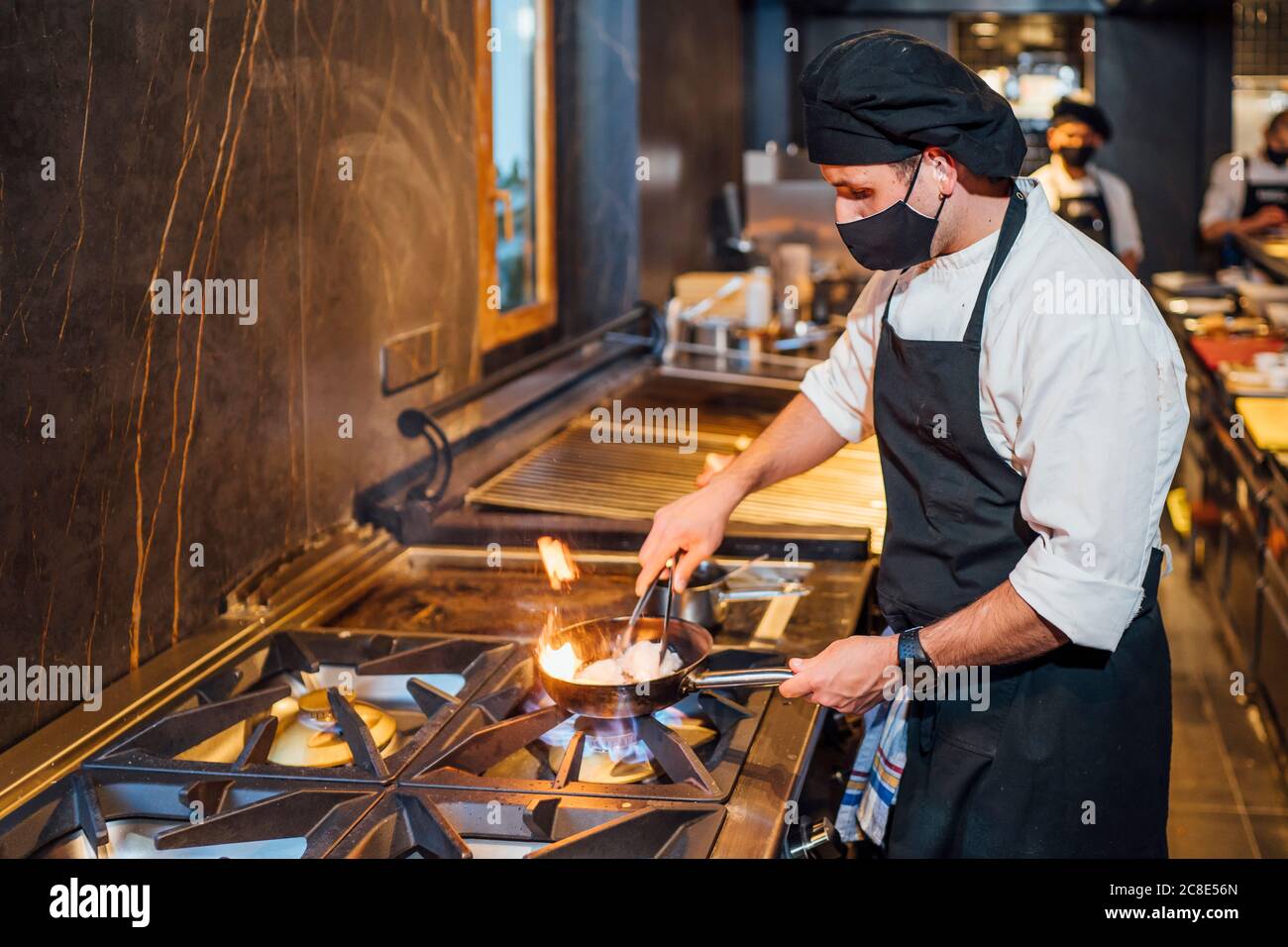 Chef wearing protective face mask preparing a dish in frying pan in