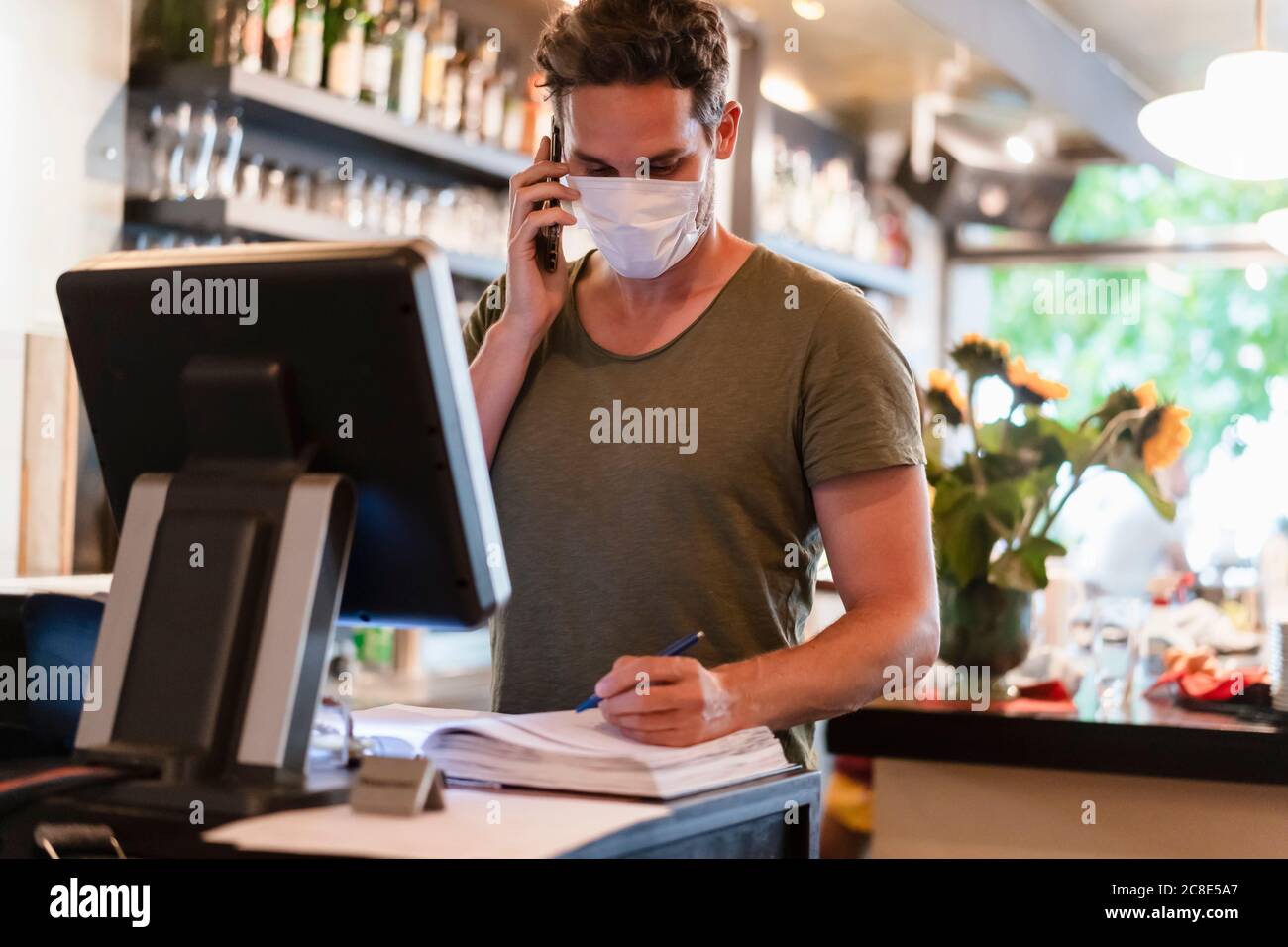 Restaurant manager with protective mask using computer and smartphone for reservation Stock Photo