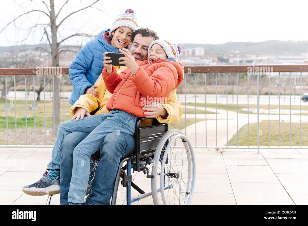 Cheerful boy taking selfie with father and brother on wheelchair in park Stock Photo