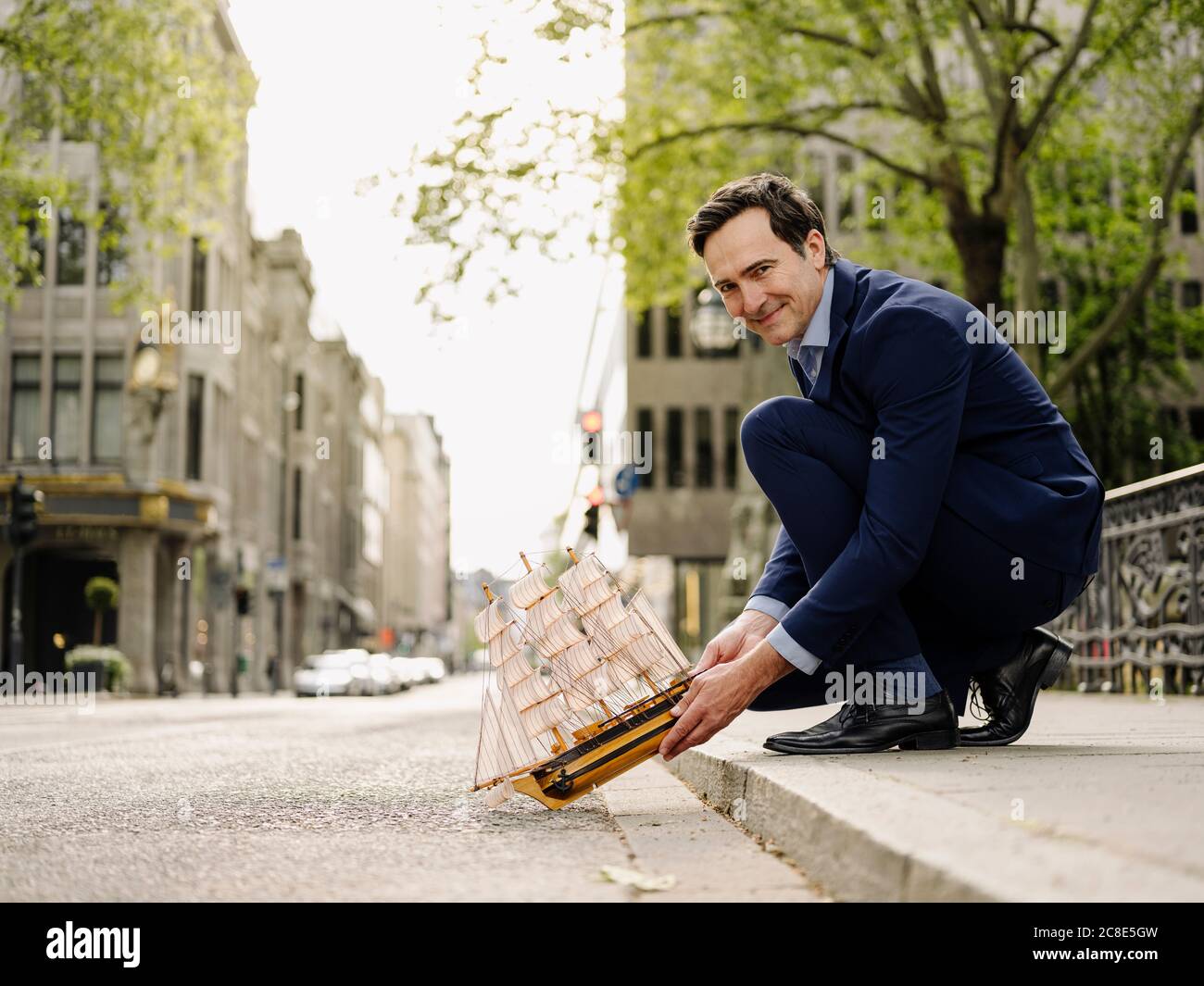 Smiling mature businessman placing model sailing ship on city street Stock Photo