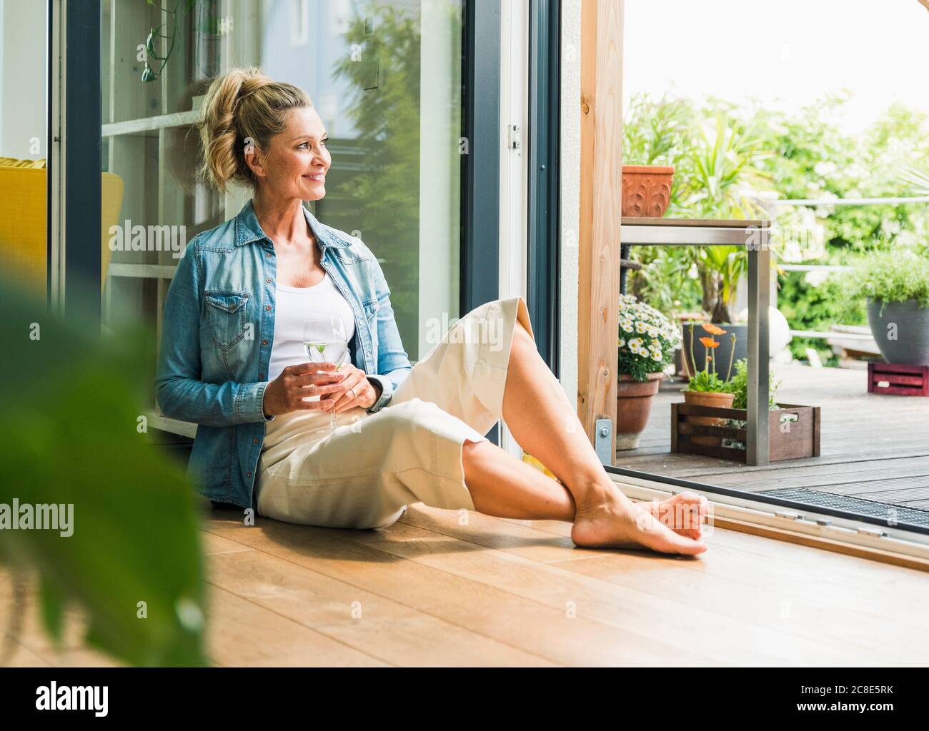 Portrait of smiling mature woman sitting on the floor at open terrace ...