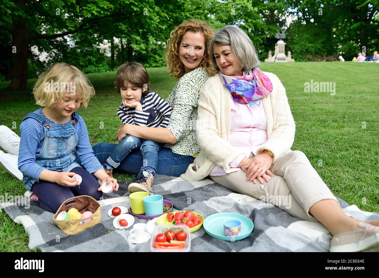 Happy children enjoying picnic with mother and grandmother at public park Stock Photo
