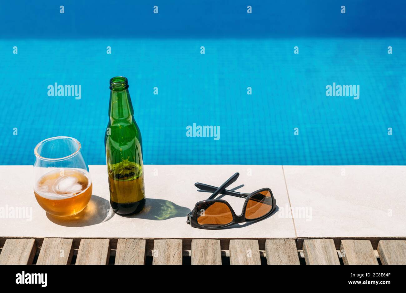Sunglasses and open beer left at edge of outdoor swimming pool in summer Stock Photo